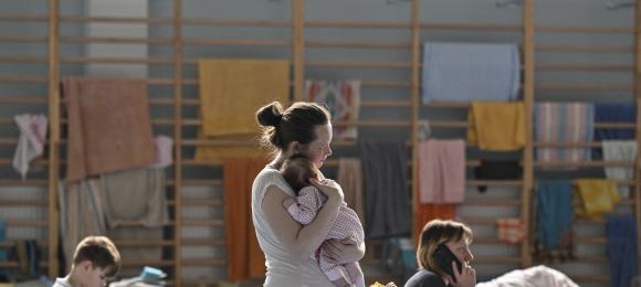 Kobieta trzyma na rękach niemowlaka, w tle łóżka, na których siedzą inne kobiety