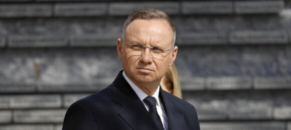 Prezydent Andrzej Duda w czarnym płaszczu i krawacie. Na nosie okulary prostokątne bez oprawek. Ma zmarszczoną twarz.