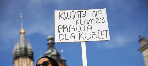 kobieta w ciemnych okularach i czarnej chustce trzyma transparent z napisem „Kwiaty na klomb, prawa dla kobiet