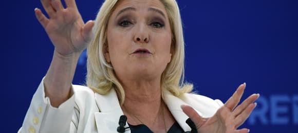 Kobieta z blond włosami macha rękami na trybunie, Marine Le Pen