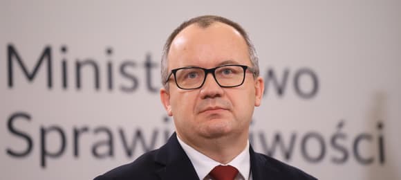 Mężczyzna w okularach na tle logo ministerstwa sprawiedliwości