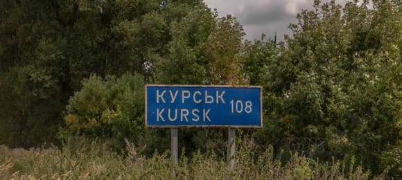 Drogowskaz z napisem Kurs 108 km na skraju drogi, na tle lasu