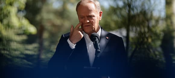 Donald Tusk mówi do mikrofonu na tle drzew