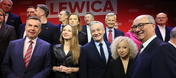 Grupa roześmianych mężczyzn i kobiet na scenie. W tle napis Lewica