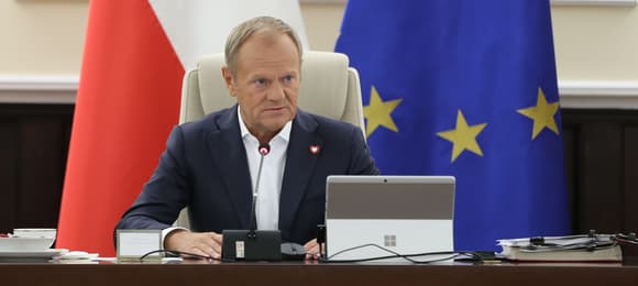 promier siedzi na tle polskiej i unijnej flagi
