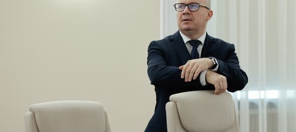 Mężczyzna w okularach stoi, oparty o wysokie krzesło
