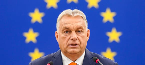 Viktor Orban sfotografowany na tle niebieskiej flagi UE; zdjęcie jest skadrowane tak, że okrąg z gwiazdek unijnej flagi układa się przy głowie premiera Węgier jak aureola.