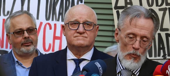 Trzech mężczyzn przed mikrofonem, w tle protest