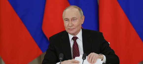 Putin na tle flag Rosji trzyma w ręku karteczki z tekstem wystąpienia dla mediów