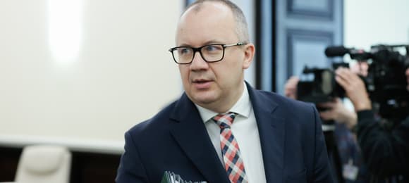Mężczyzna w okulrach, w garniturze, trzyma pod pachą plik skoroszytów