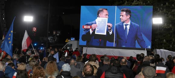 Karol Nawrocki i Rafał Trzaskowski na telebimie podczas debaty. Przed telebimem siedzą ludzie