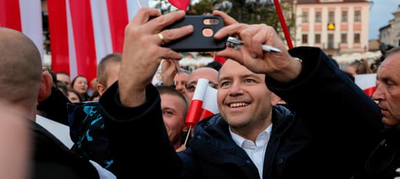 Mężczyzna stoi w tłumie i robi sobie selfie komórką trzymaną w ręku