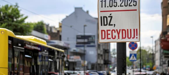 Banner referendalny na ulicy zachęcający do głosowania. W tle autobus, ulica i kamienica