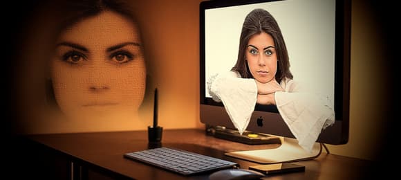 Na ekranie komputera twarz kobiety, której ręce wystają z ekranu, obok na ścianie wyświetlona sama twarz kobiety