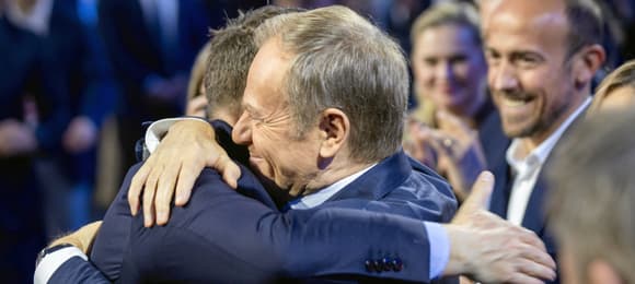 Dwaj mężczyźni w objęciach na scenie, dookoła ludzie