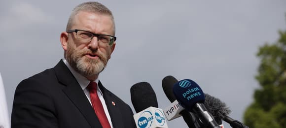 Grzegorz Braun w trakcie medialnego wystąpienia na tle pochmurnego nieba.