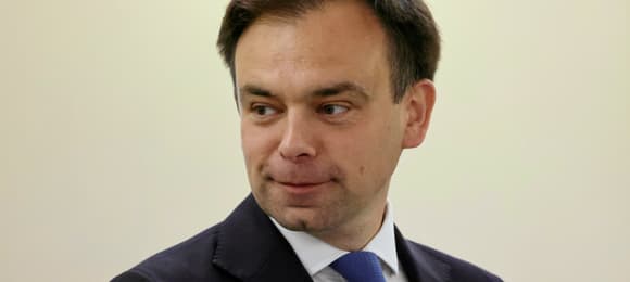 Minister finansów Andrzej Domański w garniturze na tle jasnej ściany