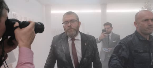 Łysawy starszy mężczyzna w okulkrach, w garniturze w chmurze gazu z gaśnicy