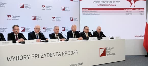 Mężczyźni w garniturach siedzą przy długim stole z napisem 