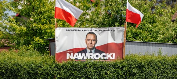 Plakat Karola Nawrockiego na żywopłocie z dwoma biało-czerwonymi flagami