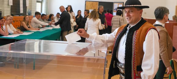 Mężczyzna w tradycyjnym góralskim stroju stoi przy urnie wyborczej