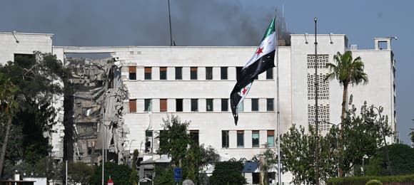 Dziura po izraelskim pocisku w budynku syryjskiego ministerstwa obrony, na pierwszym planie także poszarpana flaga Syrii