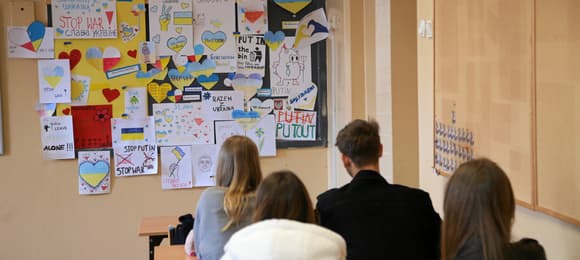 Na zdjęciu jest szkolna klasa, za ławkami siedzi czterech nastolatków (trzy dziewczyny i chłopiec). Siedzą tyłem do kamery