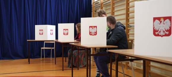 osoby siedzą za zasłonkami i wypełniają karty wyborcze