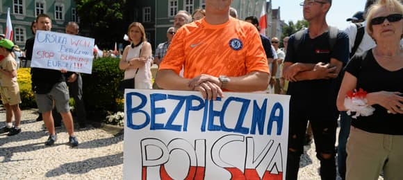 Mężczyzna w pomarańczowej koszulce trzyma transparent z napisem 