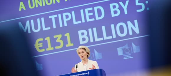 Kobieta o jasnych włosach, ubrana w biały żakiet, przemawia przy mównicy Komisji Europejskiej na tle dużego ekranu z napisem: „Unia, która chroni – zwielokrotnione 5 razy: 131 miliardów euro”.