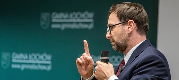 Gestykulujący 40-latek w okularach i z trzydniowym zarostem.