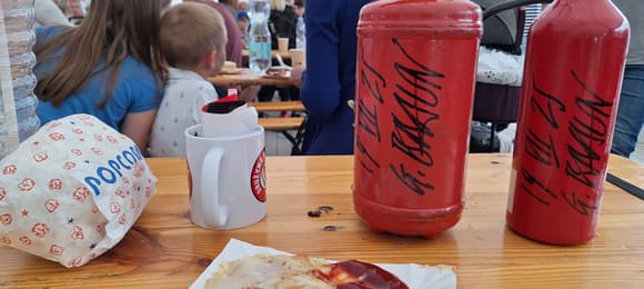 Na stole leży plastikowy talerzyk z resztkami po ketchupie, obok dwie gaśnice z autografem Grzegorza Brauna.