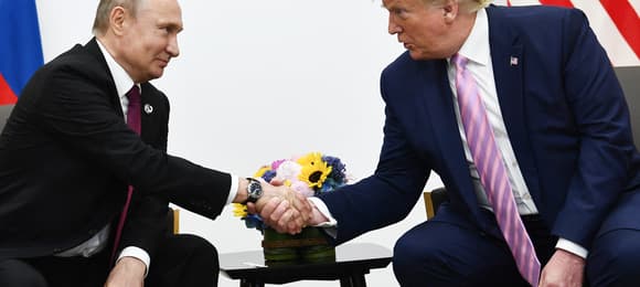 Dwaj mężczyźni w garniturach siedzący przy stoliku podają sobie ręce.