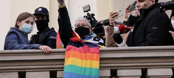 Kobieta z poniesioną ręką pokazuje symbol zwycięstwa, obok niej tłum i policja