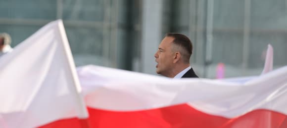 Nad białoczerwonymi flagami wystaje głowa mężczyzny