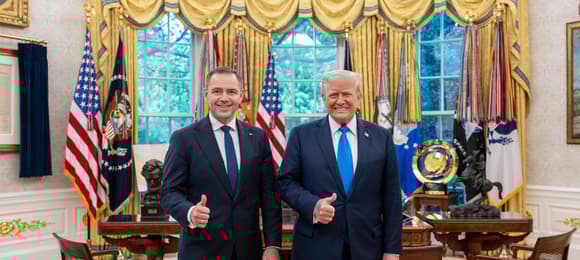 Dwóch mężczyzn w garniturach i niebieskich krawatach, jeden w średnim wieku (Karol Nawrocki), drugi starszy (Donald Trump) uśmiecha się szeroko podnosząc kciuk do góry w wytwornie urządzonej sali (Gabinet Owalny w Białym Domu)