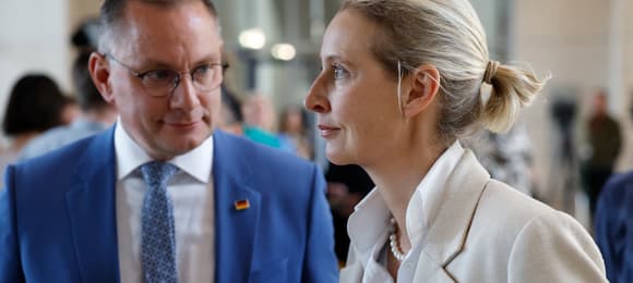 Mężczyzna w niebueskiej marynarce i jasnowłosa kobieta w beżowej garsonce