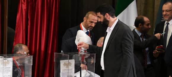 Mężczyźni w garniturach i z brodami wrzucają głosy do urn.