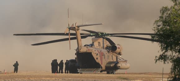 Helikopter wojskowy na pustyni. Obok widać małą grupkę ludzi