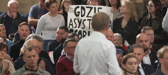 Premier i grupa ludzi. Młode kobiety trzymaja transparent z napisem 