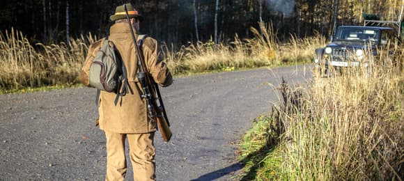 myśliwy w bronią stoi tyłem do aparatu