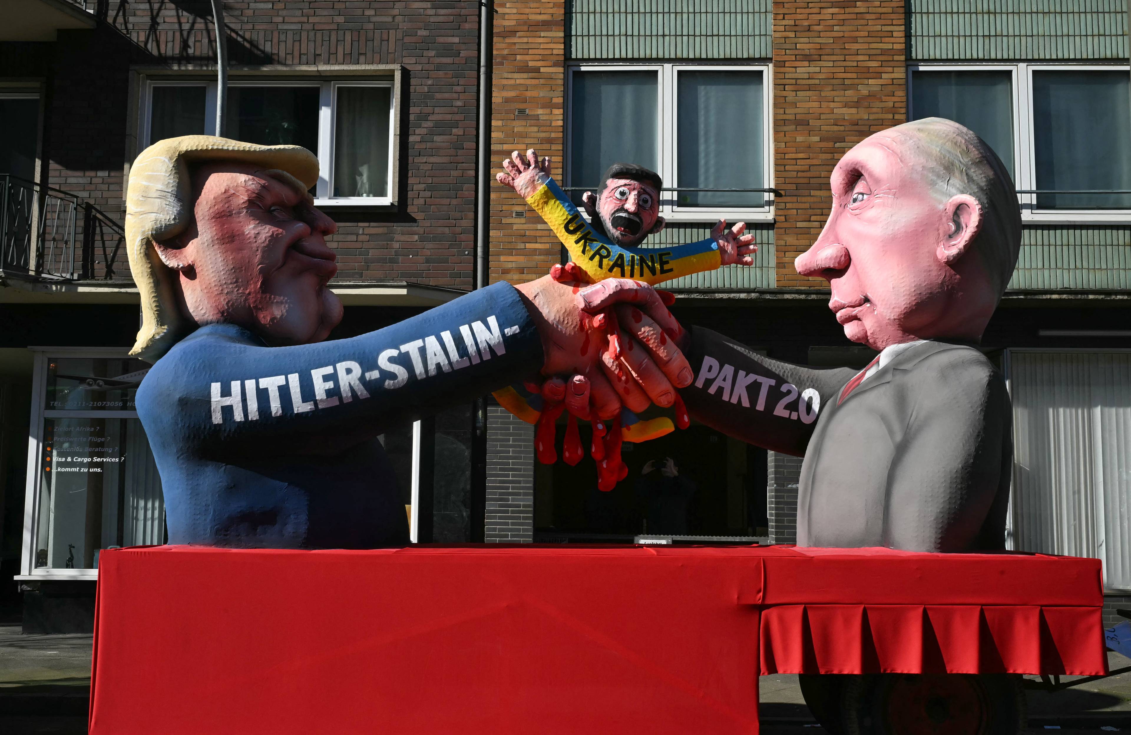 Dwie kukły satryczne przedstawiają Trumpa i Putina, którzy zaciskają dłonie na kukle Ukrainy. Na rękawie kukły Trumpa napis "Hitler Stalin"