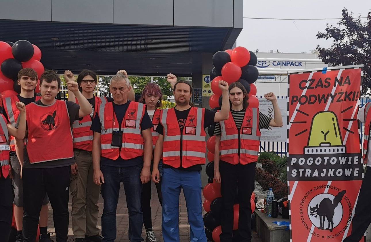 Strajkujący pracownicy w pomarańczowych kamizelkach przed fabryką