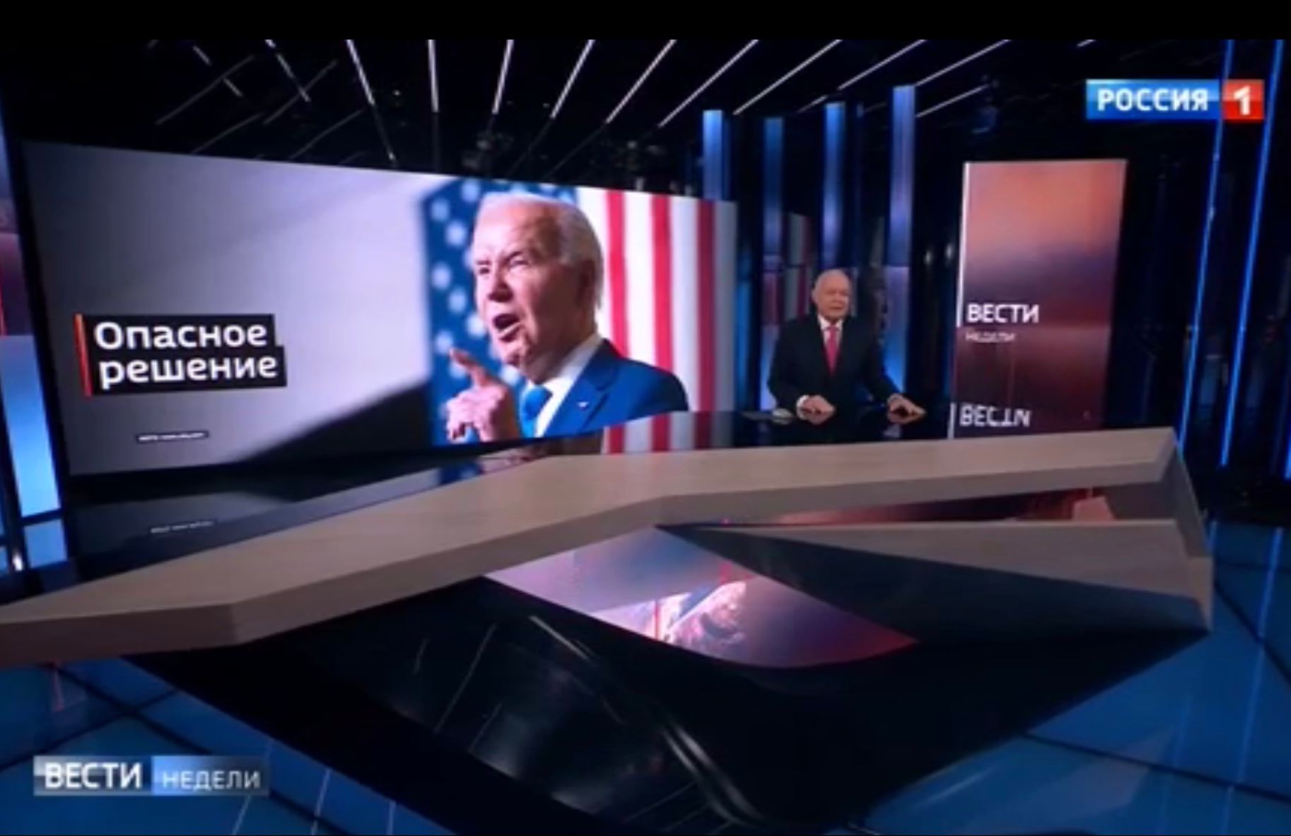 Studio telewizyjne. Prezenter na tle wielkiego zdjęcia prezydenta Bidena i rosyjskiego napisu "Niebezpieczna decyzja"