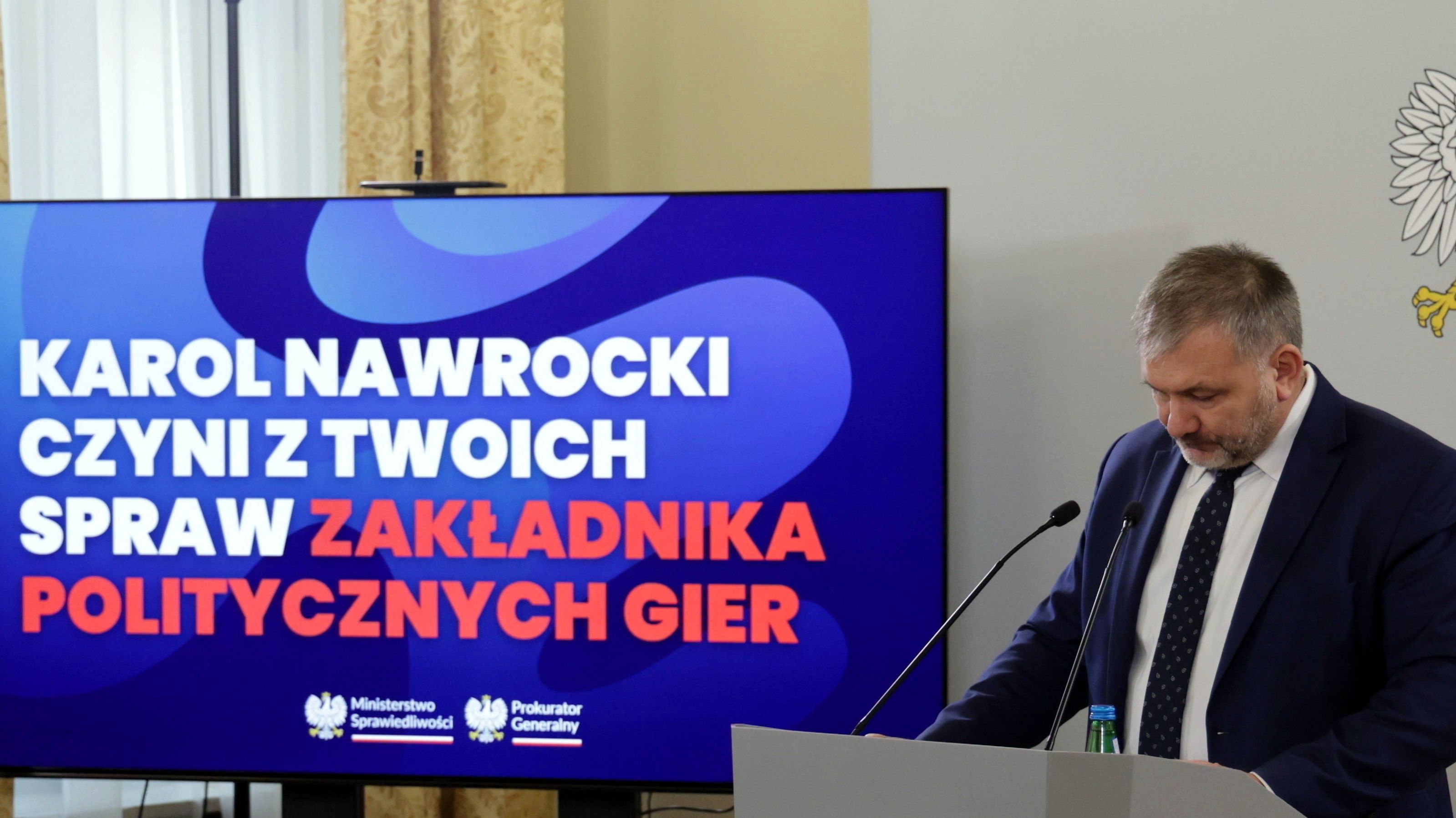 Mężczyzna w garniturze stoi na mównicy, za nim Napis Karol NAwrocki czyni z twoich spraw zakładnika politycznych gier