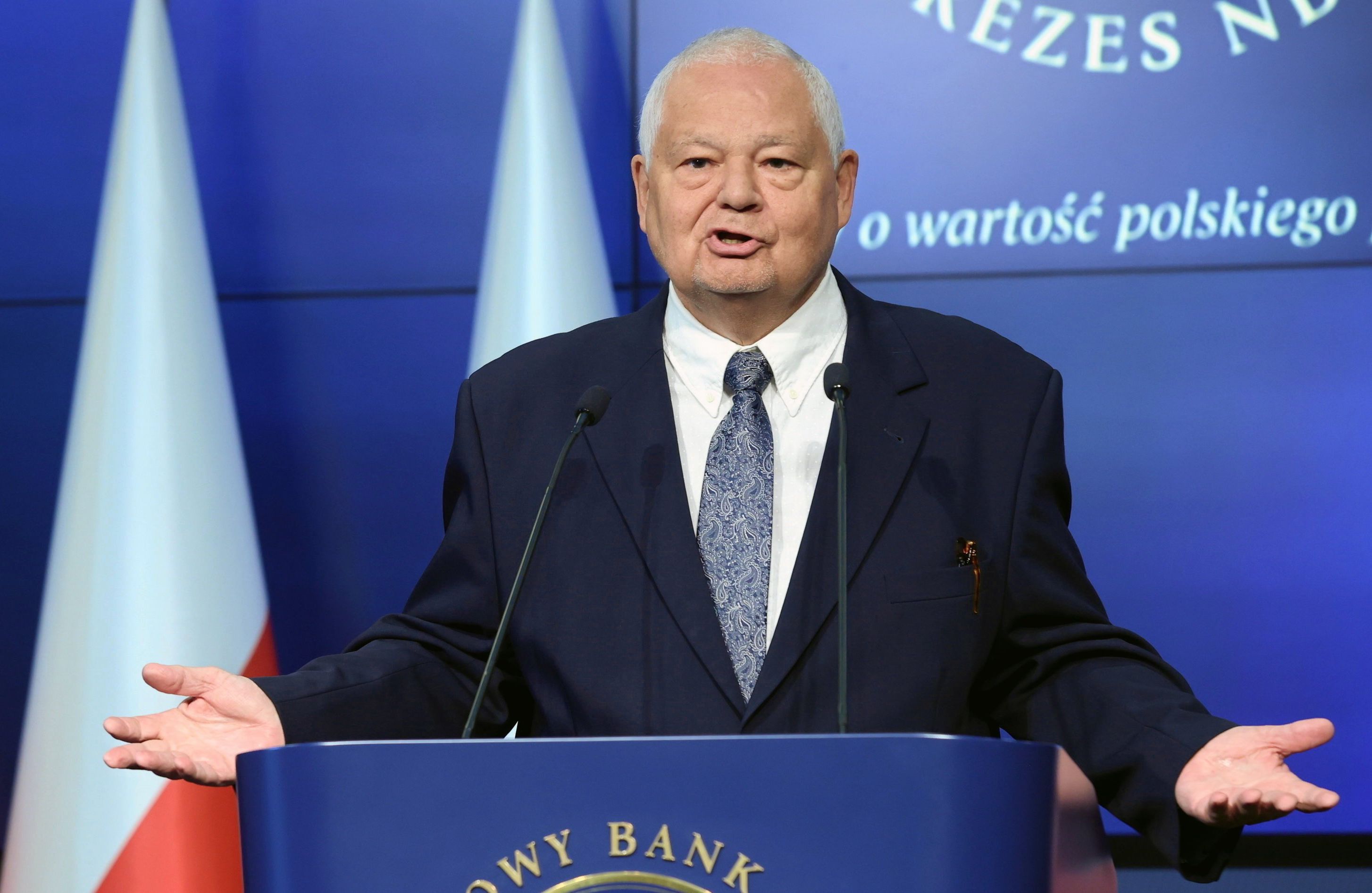 Prezes NBP Adam Glapiński przemawia na konferencji prasowej przed pulpitem
