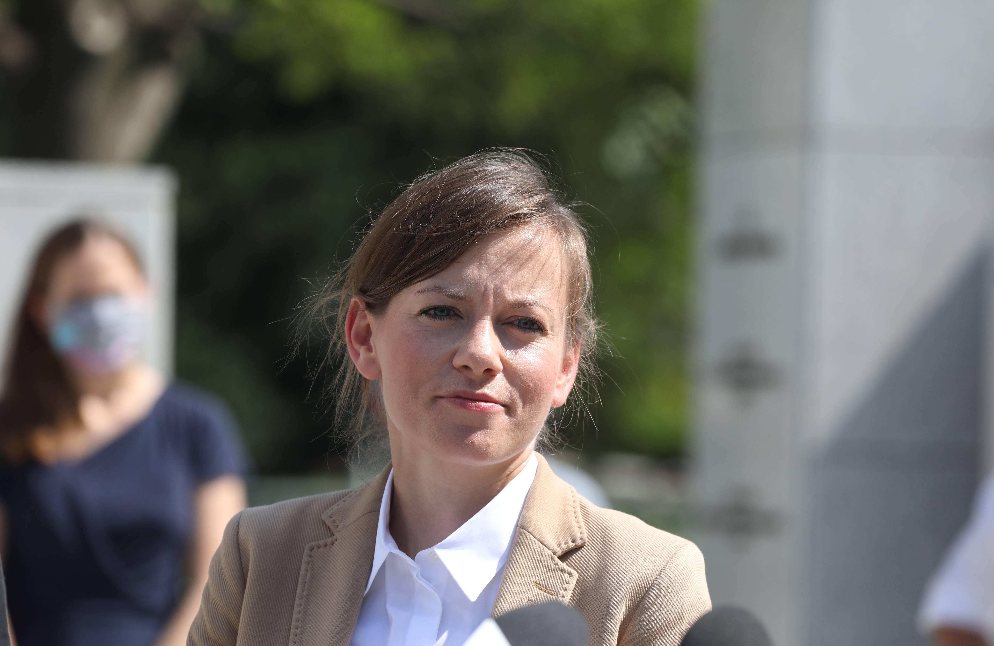 młoda kobieta z upiętymi włosami, w białej bluzce i beżowej marynarce