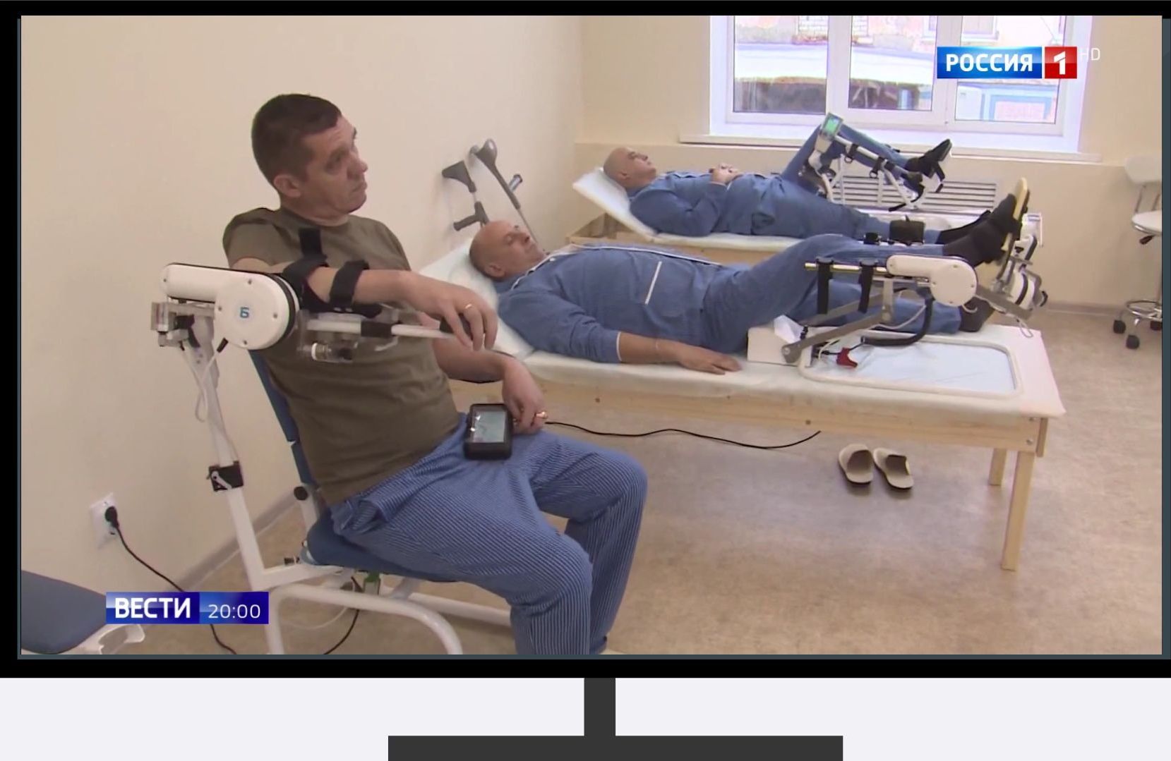Screen w ramce telewizora: Ranni zołnierze w czystych piżamach ćwiczą na łózkach