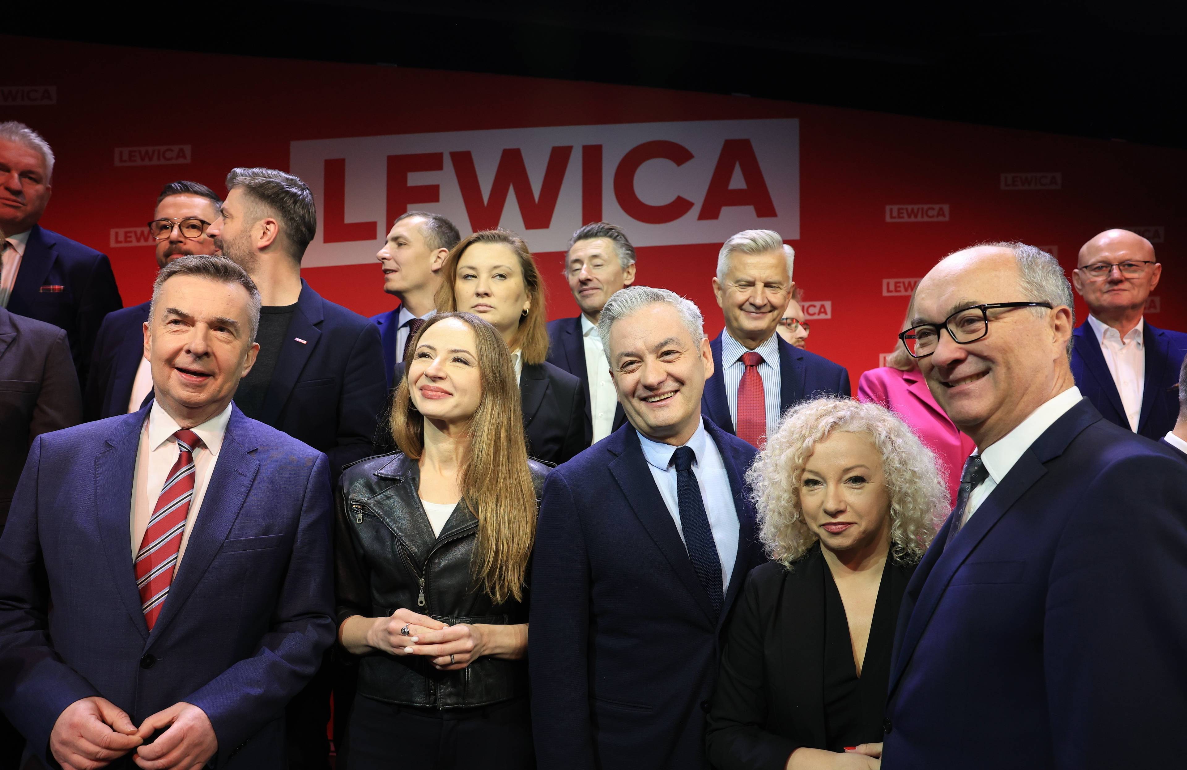Grupa roześmianych mężczyzn i kobiet na scenie. W tle napis Lewica