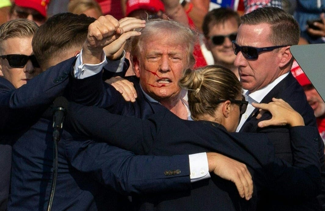 Donald Trump na wiecu, tu po zamachu, podnosi w górę pięść w otoczeniu ochroniarzy